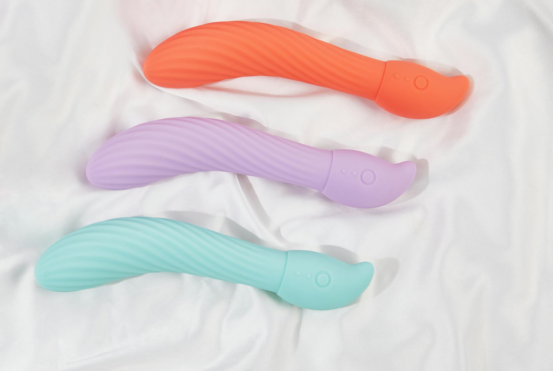 Three colorful vibrators arranged on white fabric, showcasing texture and design