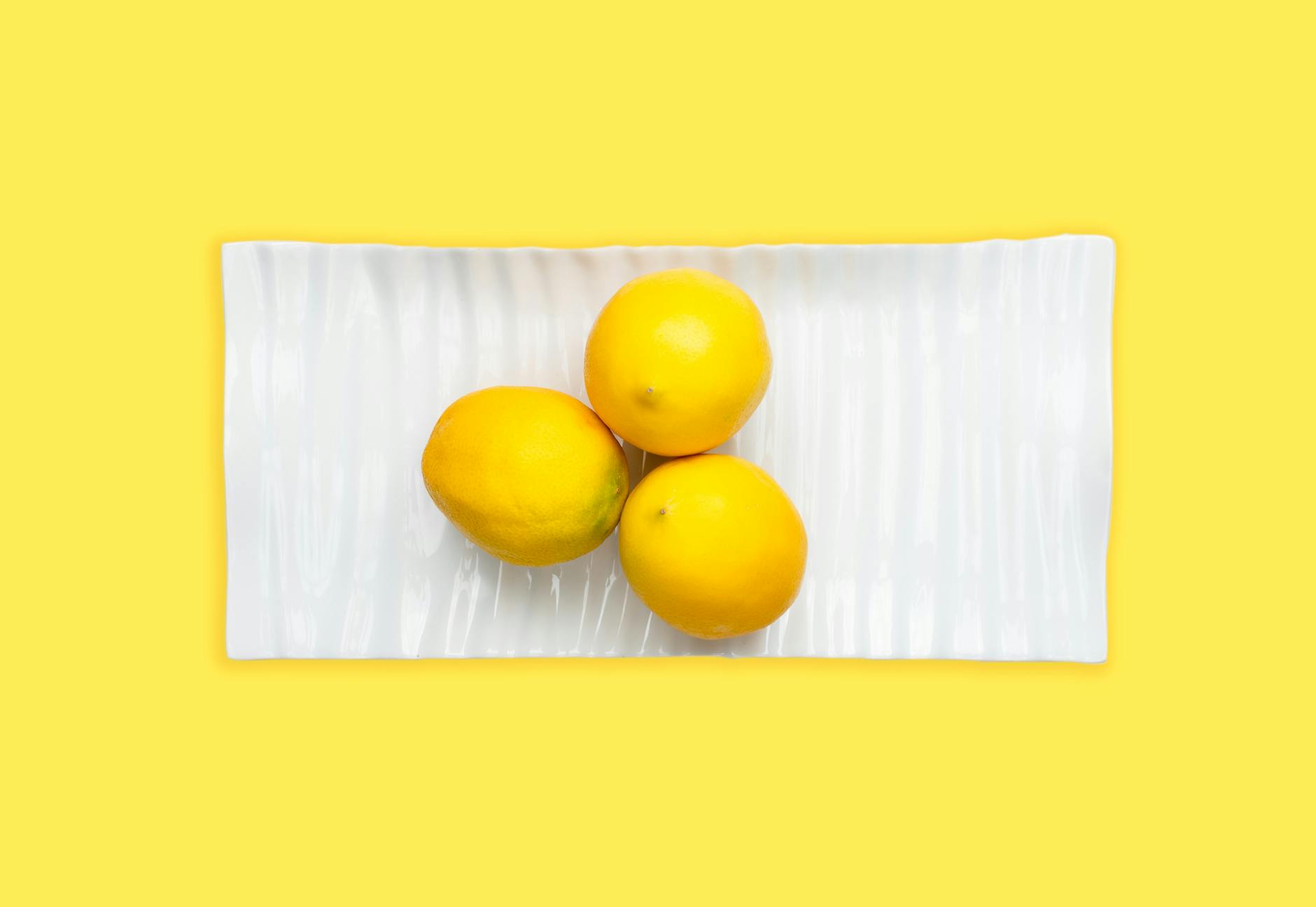 Three fresh lemons arranged on a white plate with a vibrant yellow background, symbolizing the science of sensation design.