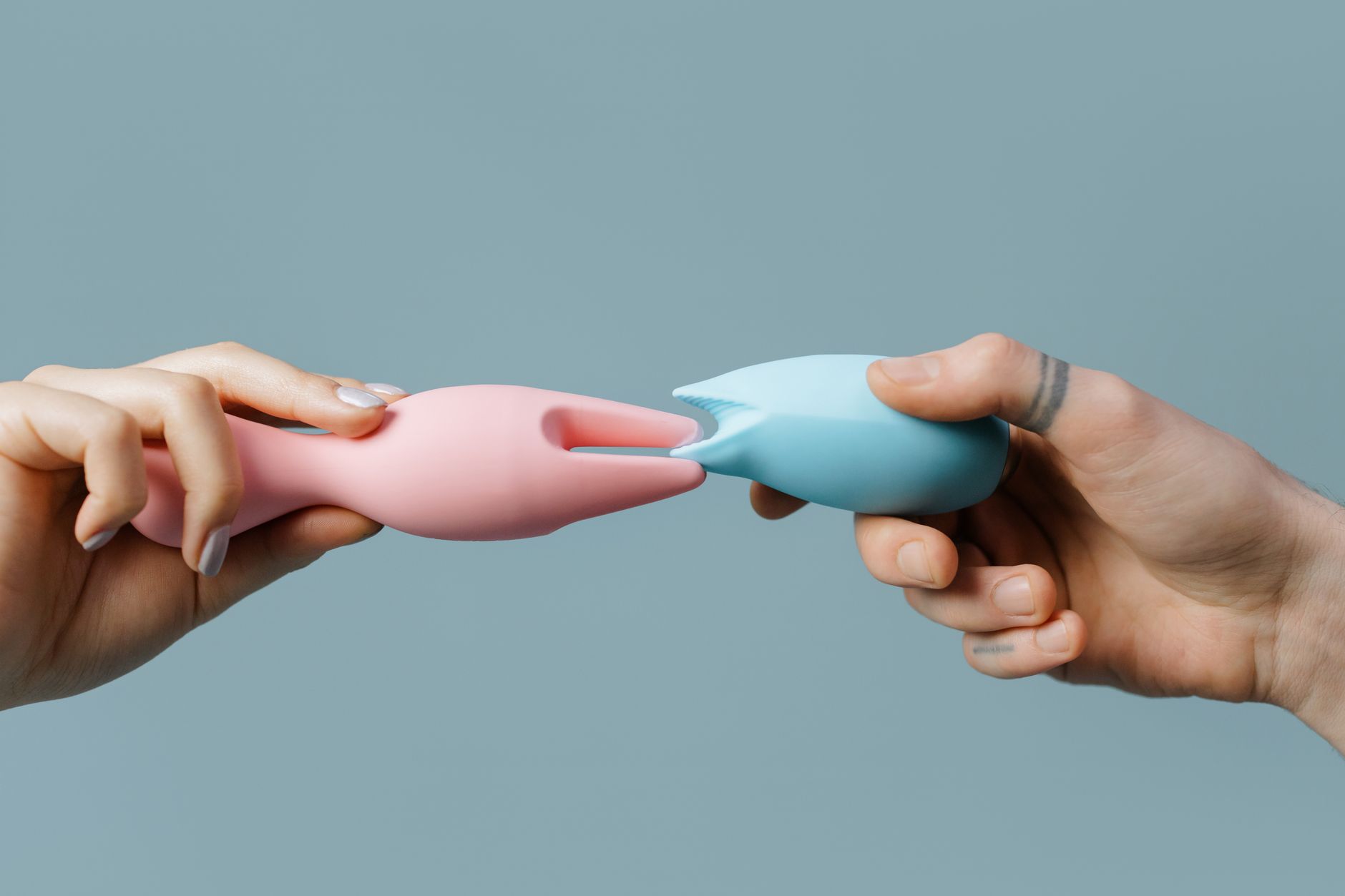 A hand reaching over a variety of colorful sex toys including lemon clitoral vibrators arranged on a table.