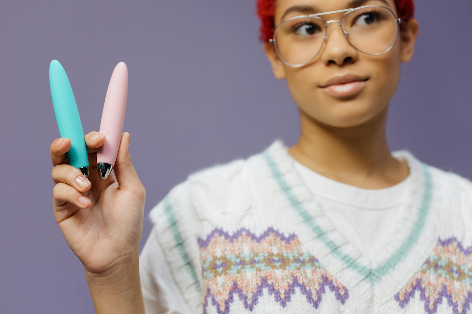 A person holding colorful vibrators against a purple background, demonstrating variety and choice