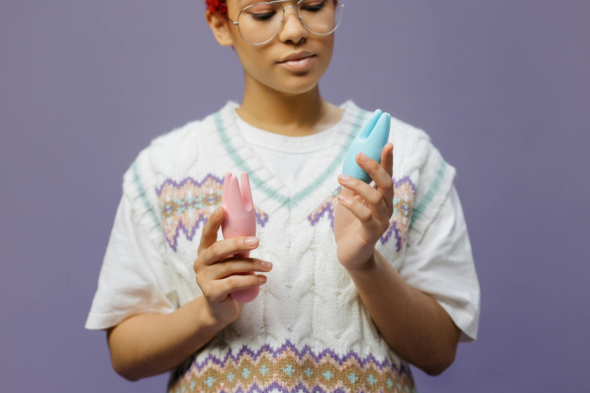 Woman holding blue and pink silicone vibrators in contemplative moment.